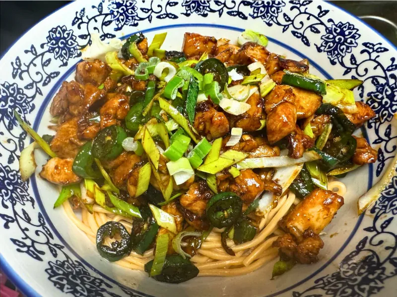 Noodle dish topped with savory chicken and greens at Chef Zhang Cuisine & Bar, a Chinese Restaurant in Cambridge
